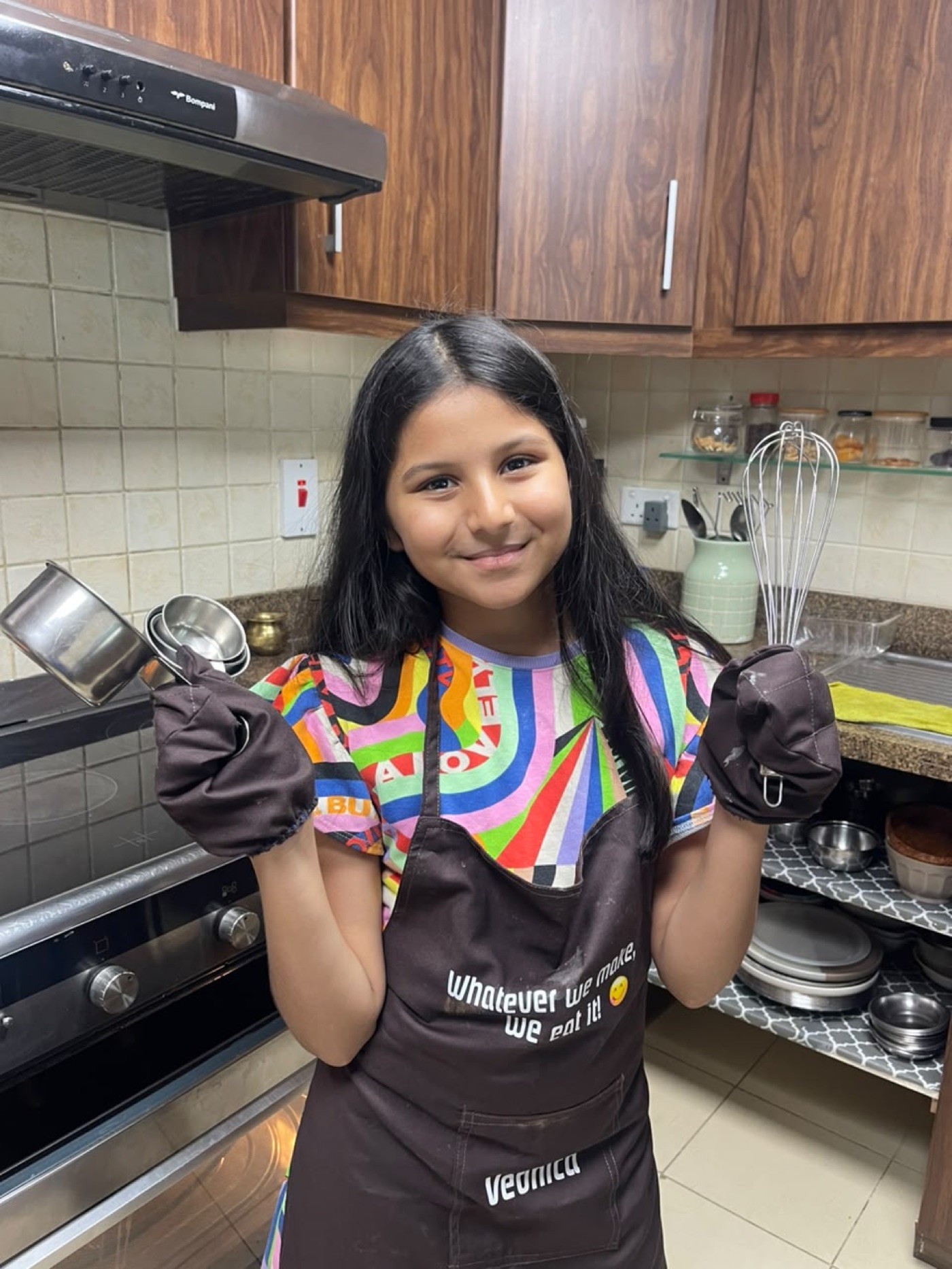 Vedhica in her apron holding a whisk and measuring cups in the kitchen