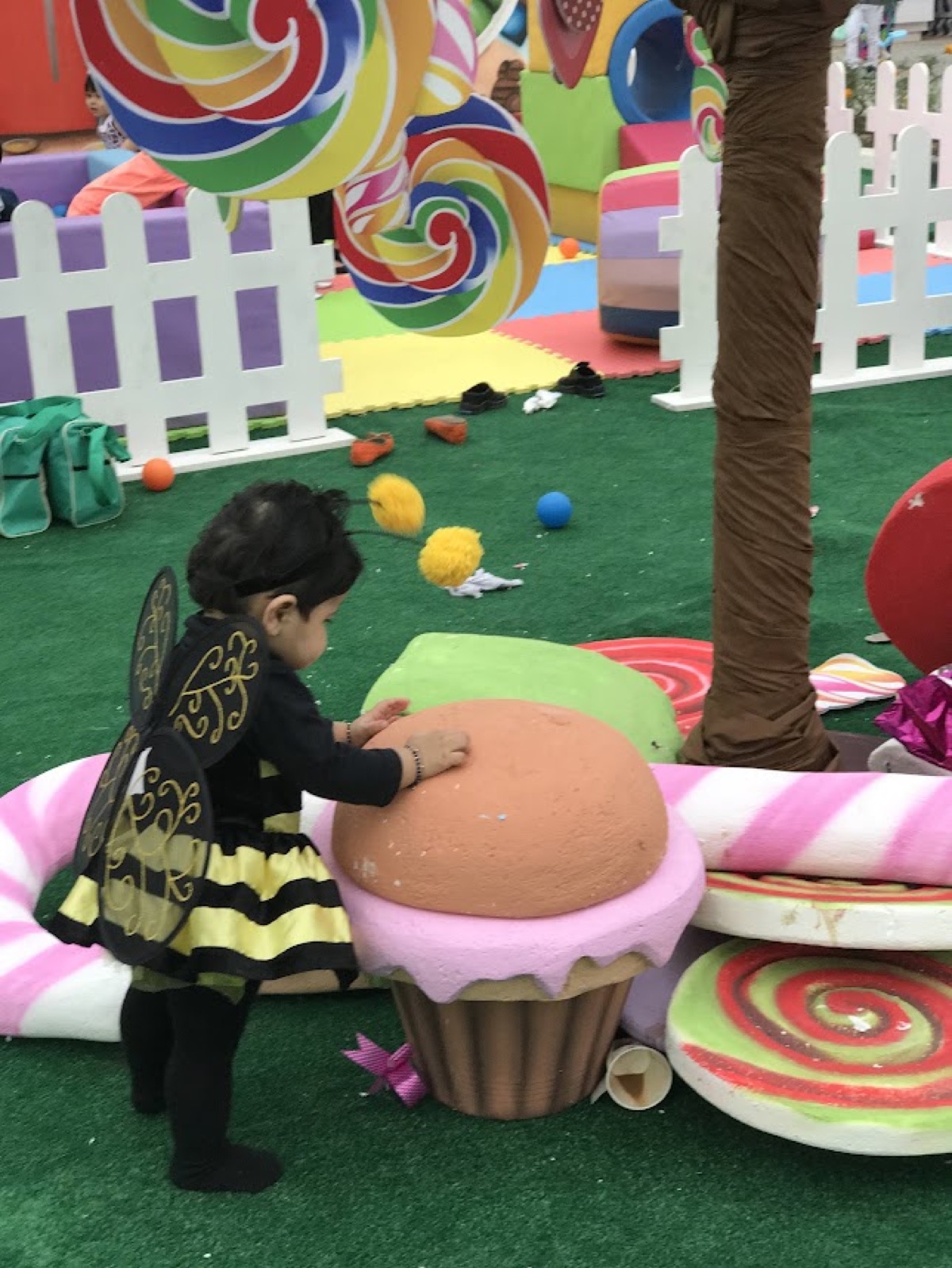Toddler Vedhica in a bee costume reaching for a giant cupcake sculpture at a candyland event