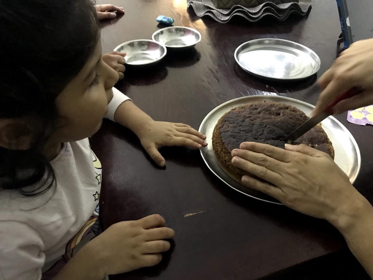 Young Vedhica watching closely as a darker-baked cake is cut at the table