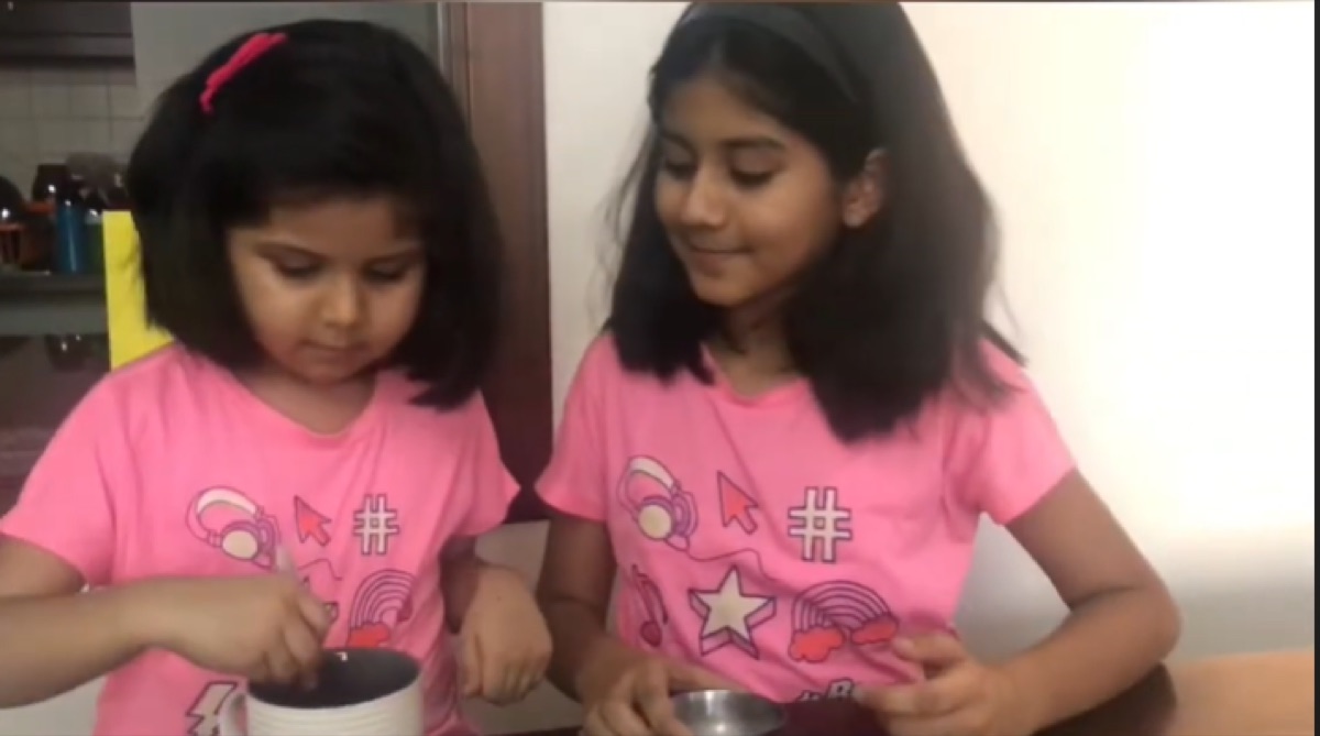 Vedhica and her sister in matching pink t-shirts mixing a mug cake together