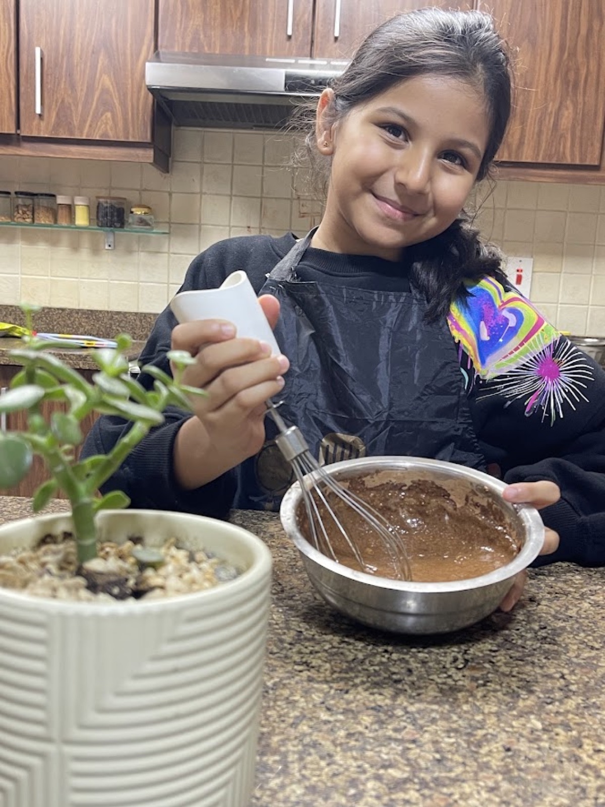 Vedhica smiling over a metal bowl of chocolate batter in the kitchen