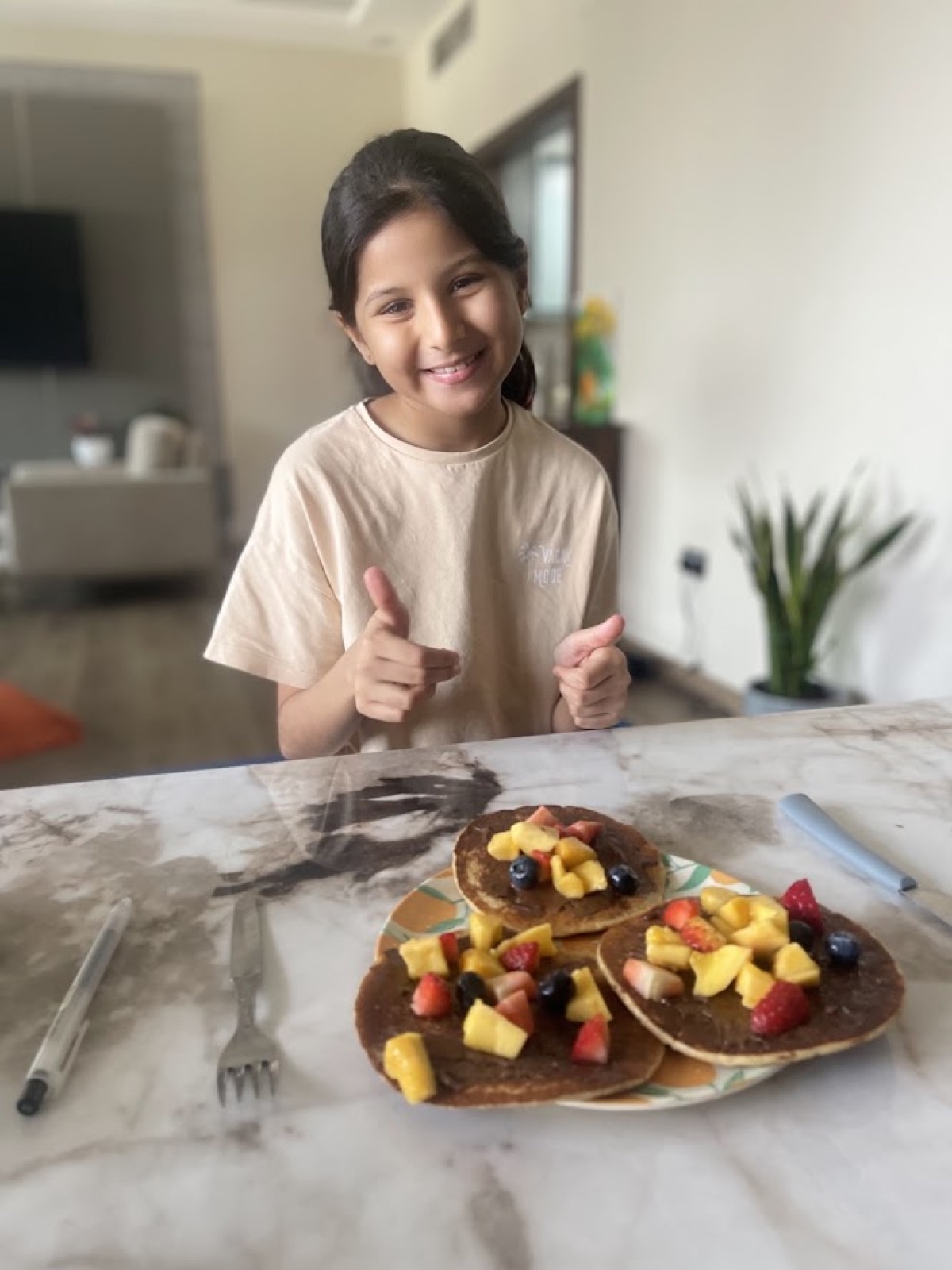 Vedhica smiling behind a plate of pancakes topped with mango, strawberries and blueberries