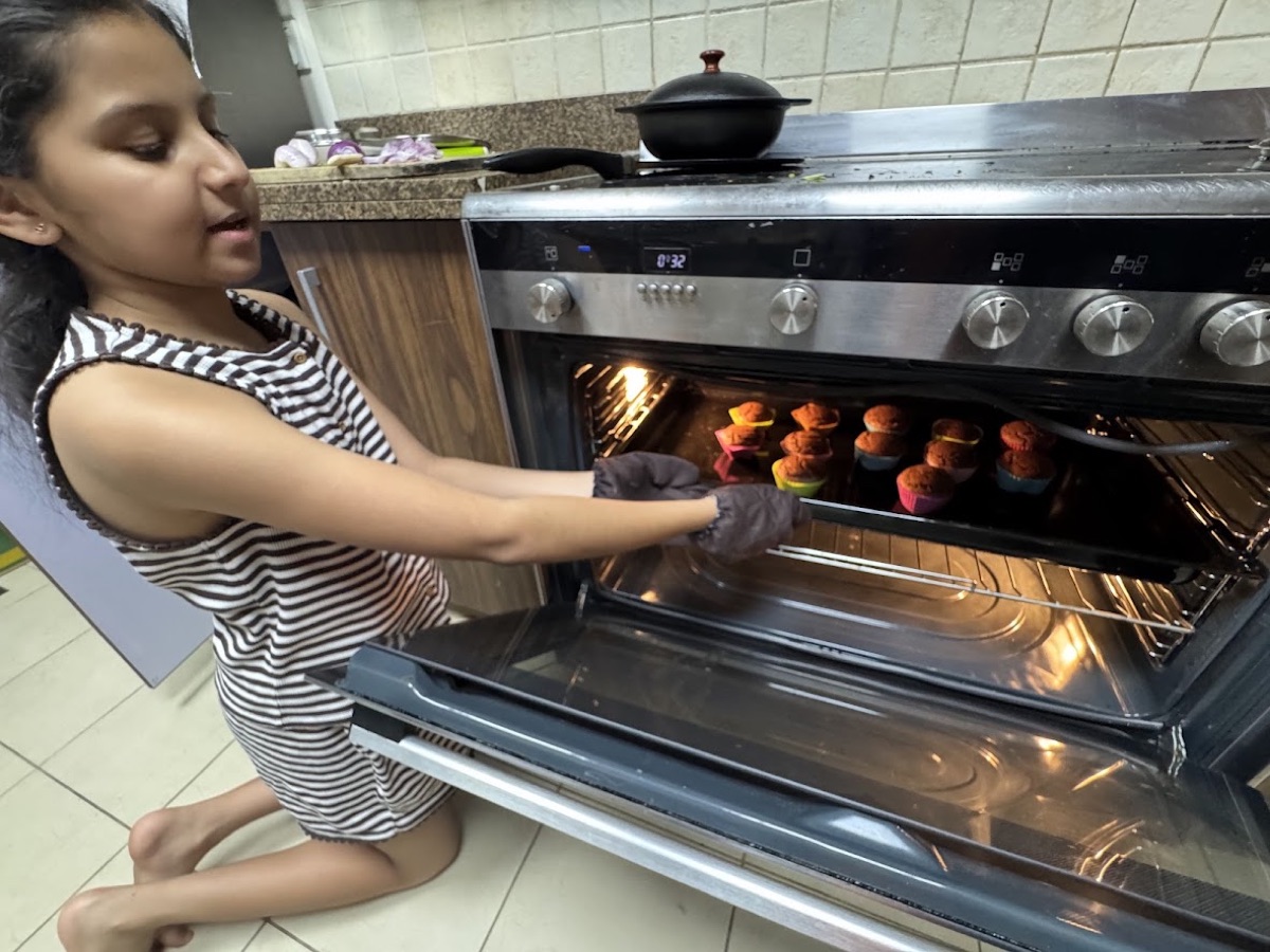Vedhica taking a tray of cupcakes out of the oven