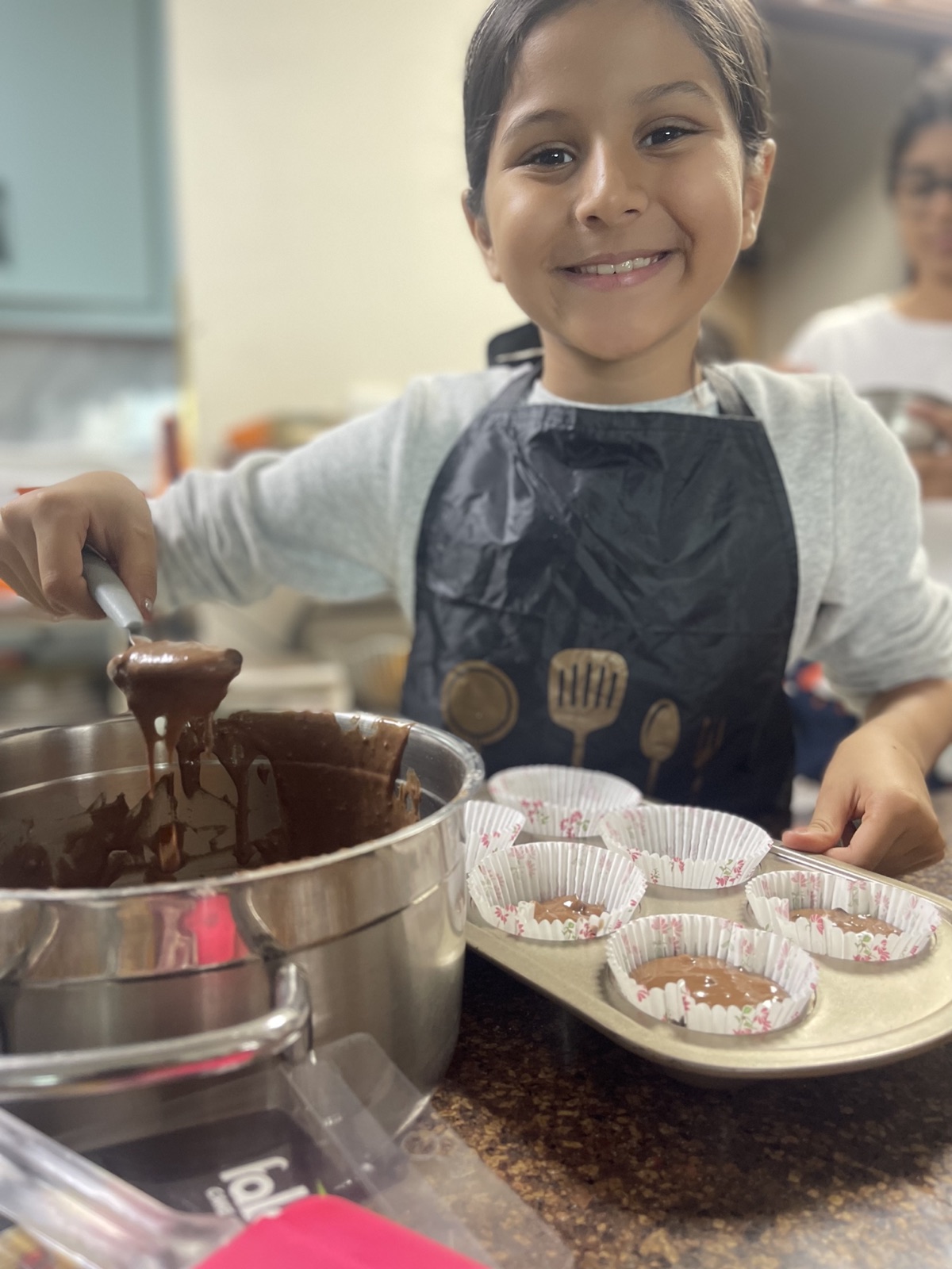 Vedhica smiling as she spoons chocolate batter into cupcake liners